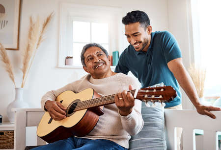 He loves listening to his dad play. Shot of a young man listening to his father play the guitar at home.の写真素材