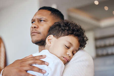 Mixed race boy sleeping on his dads shoulder. Boy feeling safe in fathers arms. Father holding his...