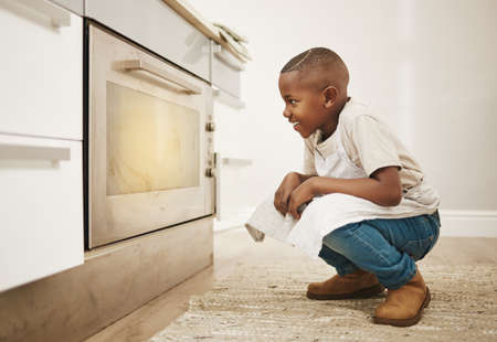 Cant wait to taste these. Shot of a little boy watching his baked goods cook in the oven at home.の写真素材