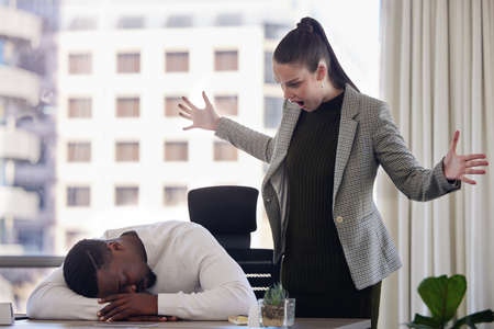 Why are you sleeping. Shot of a young female boss looking angry while a coworker sleeps in an office at work.の写真素材