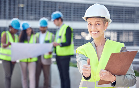 Well have this project completed in no time. Cropped portrait of an attractive female construction worker giving thumbs up while standing on a building site with her colleagues in the background.の写真素材
