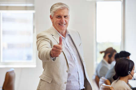 Leave the hard work to my team. Shot of a mature businessman standing in the office and showing a thumbs up.の写真素材