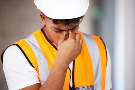 Ill need a painkiller. Shot of a young contractor suffering from a headache while working.の写真素材