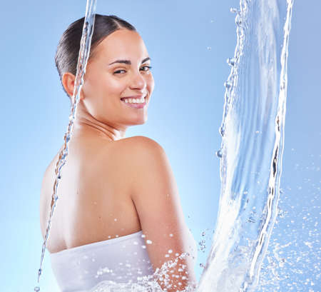 Water babe. Shot of a beautiful young woman enjoying a refreshing shower against a blue background.の写真素材