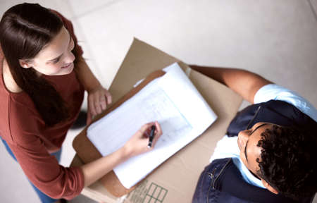 Sign on the dotted line. Shot of a young woman signing for her delivery.