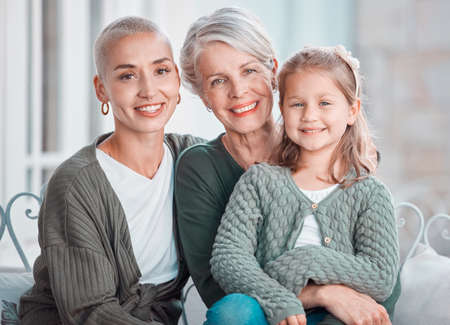 Portrait of three generations of females looking and smiling at the camera. Adorable little girl bonding with her mother and grandmother at homeの写真素材