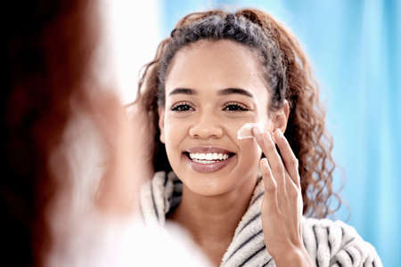 My face loves love. Cropped shot of an attractive young woman applying lotion to her face in the bathroom at home.の写真素材