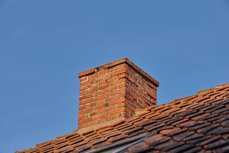 Copy space with a chimney on the rooftop of a house or building against a blue sky background. Brick construction of an exterior escape chute for ventilation of air and smoke from a fireplace or ovenの写真素材