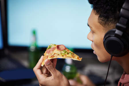 Eat, sleep, game, repeat. Closeup shot of a young man eating pizza while playing video games at home.の写真素材