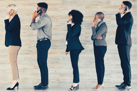 There is no traffic jam along the extra mile. Shot of a group of businesspeople waiting in line and using a phone at an office.の写真素材