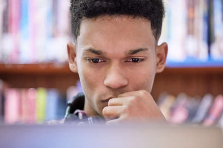 Dedication and discipline make a powerful combo. Shot of a young man using a computer in a library at university.の写真素材
