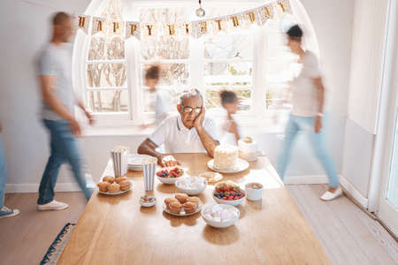 The soul that sees beauty may sometimes walk alone. Shot of a senior man looking lonely while celebrating his birthday alone at home.の写真素材