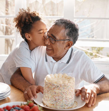 Your birthday is the beginning of your personal new year. Shot of a Grand daughter kissing her grandpa during a birthday party at home.の写真素材