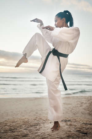 You dont want to mess with her. Shot of a young martial artist practising karate on the beach.の写真素材