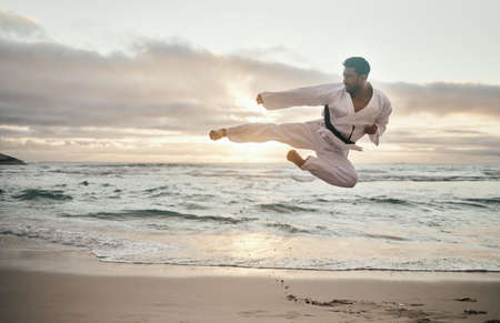 Keep calm and kick on. Shot of a young martial artist practising karate on the beach.の写真素材