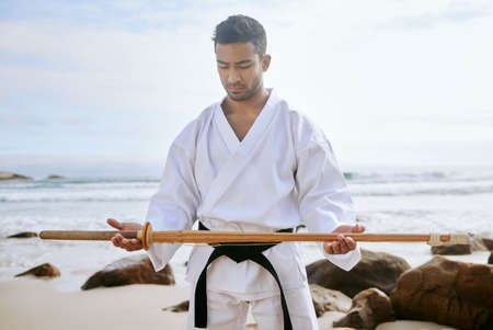Warriors are always ready for anything. Shot of a young martial artist practising karate with a wooden katana on the beach.の写真素材