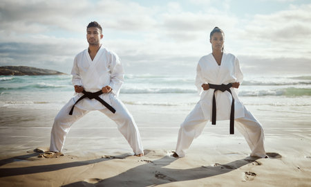 Ready for a fight. Full length shot of two young martial artists practicing karate on the beach.の写真素材