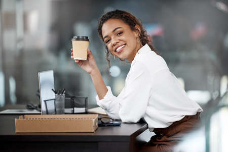Cheers to success. Cropped portrait of an attractive young businesswoman working at her desk in the office.の写真素材