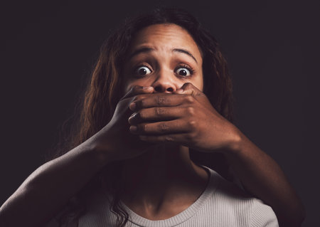 You wake up every morning to fight the same demons. Shot of a scared young womans mouth being covered by an unrecognisable mans hand against a black background.の写真素材