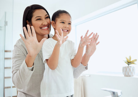 We covered every finger. Shot of an adorable little girl washing her hands while her mother helps at home.の写真素材