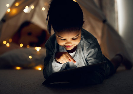 What should I watch next. Shot of a little girl using a digital tablet late at night at home.の写真素材