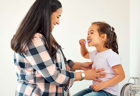 I can do it myself, mom. Shot of a mother helping her little daughter brush her teeth in the...