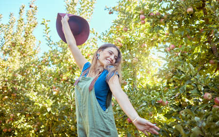 Excited young woman jumping for joy in an apple orchard on a sunny day outside. Happy and cheerful...