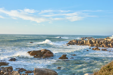 Copyspace at sea with a cloudy blue sky background and rocky coast in Western Cape South Africa....