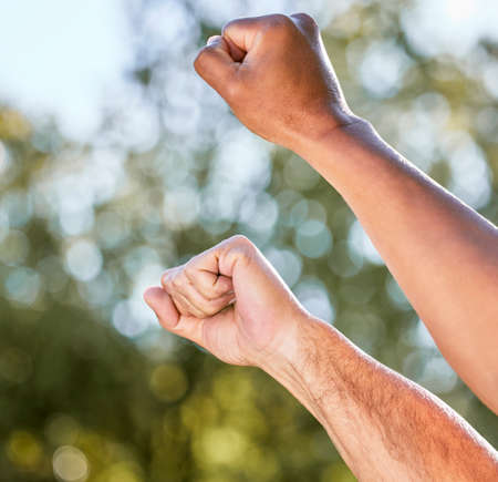 Keep fighting on. Shot of two unrecognisable men raising their fists in defiance outdoors.