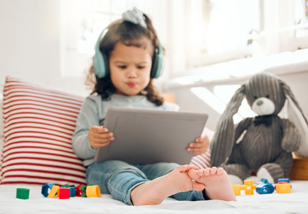 Shes in a world of her own. Shot of an adorable little girl sitting on her bed with a digital tablet.の写真素材