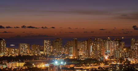 High rise, skyscrapers lit up at night in a city with small houses in the foreground night beautiful modern buildings and bright glowing lights. The blue twilight skyline in the metropolis.の写真素材