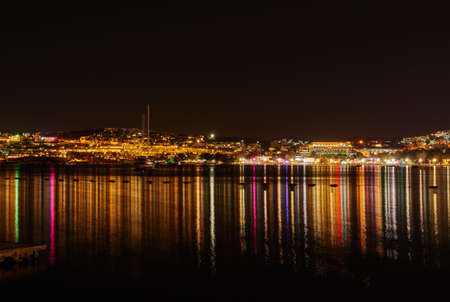 City lights reflecting on water with dark sky copy space. River or lake at night with beach house light reflections on water surface. Colorful midnight skyscraper glowing in still water near a harborの写真素材
