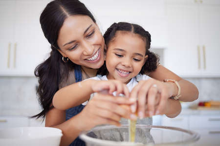Happy mother and daughter bonding, baking in a kitchen at home. Smiling single mother teacher her...