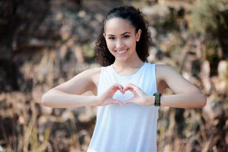 Do whatever keeps your heart healthy. a sporty young woman forming a heart shape with her hands while standing outside.の写真素材