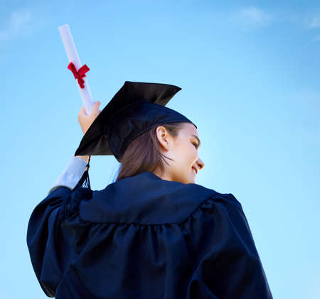 Set sail towards your dreams. Low angle shot of a young woman cheering with her diploma on graduation day.の写真素材