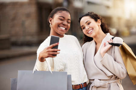 When the sun comes out so do the shoppers. two young women taking selfies while shopping against an urban background.の写真素材