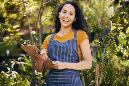 I have some checks to do. a young female florist taking notes while examining plants at work.の写真素材