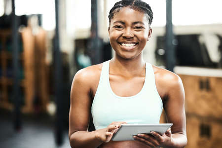 Ready to get fit. an attractive young woman standing alone in the gym and using a digital tablet.の写真素材
