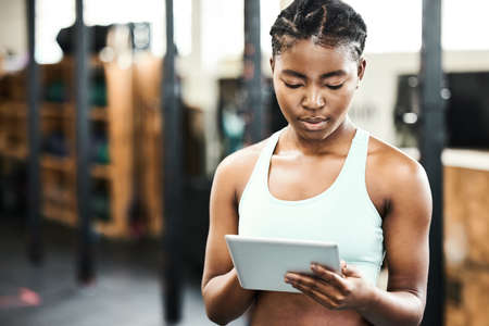 Im in for a tough workout. an attractive young woman standing alone in the gym and using a digital tablet.の写真素材