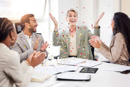 This deserves some celebration. a mature businesswoman sitting with her colleagues and throwing confetti to celebrate a success during a meeting.の写真素材
