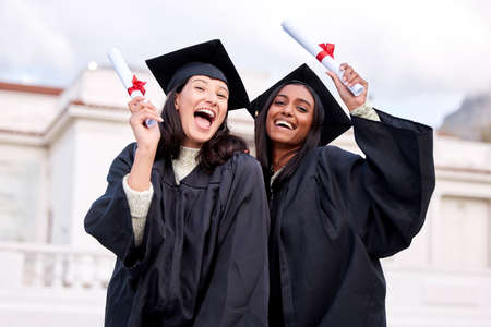 Guess what we did. Portrait of two young women celebrating with their diplomas on graduation day.の写真素材