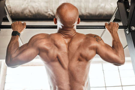 This back shoulders the weight of the world. a man completing pull ups in his gym.