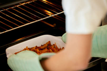 Its ready to go. an unrecognizable person removing food from an oven at home.の写真素材