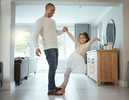 Were practicing for our first daddy and daughter ball. a little girl wearing her tutu and tiara while dancing with her father at home.の写真素材