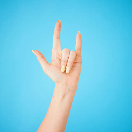 Party on my people. Studio shot of an unrecognisable woman making a horn sign against a blue background.の写真素材