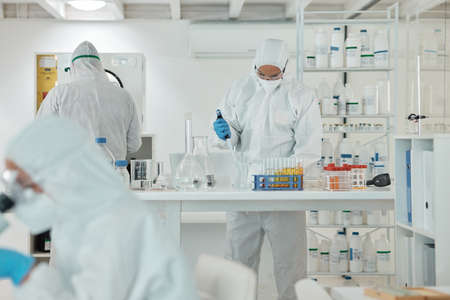 Conducting experiments under defined conditions. a scientist wearing a radiation suit while working...