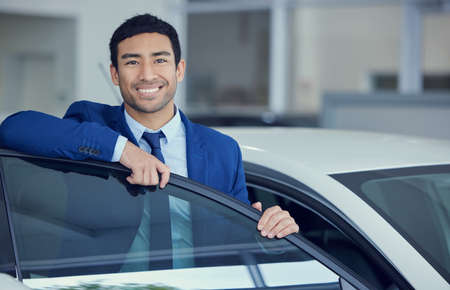 Hop on in. Cropped portrait of a handsome young male car salesman working on the showroom floor.の写真素材