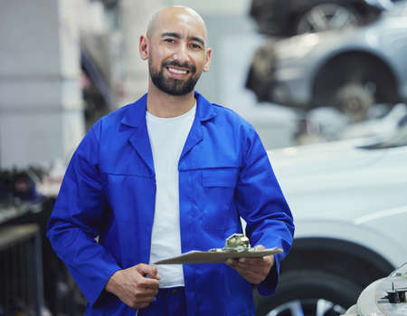 Lets assess your vehicle. Cropped portrait of a handsome young male mechanic working on the engine of a car during a service.の写真素材