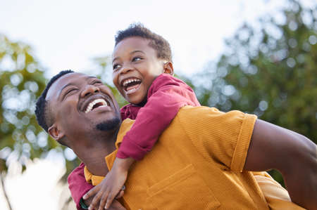 Lets go higher, dad. an adorable little boy enjoying a piggyback ride with his father in a garden.