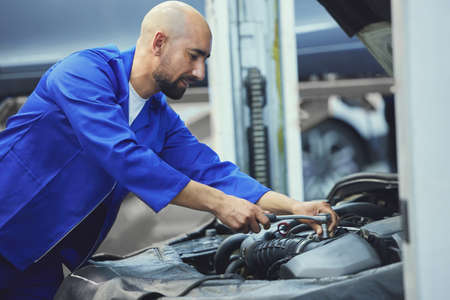 Hes an expert when it comes to engines. a handsome young male mechanic working on the engine of a...